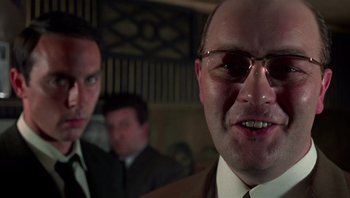 Movie still from “Performance” (1970), directed by Donald Cammell – A man in a suit and tie with glasses; Close Up shot, Low angle