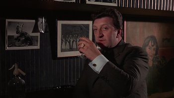 Movie still from “Performance” (1970), directed by Donald Cammell – A man holding a wine glass in his right hand; Medium shot, Low angle