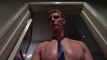 Movie still from “Performance” (1970), directed by Donald Cammell – A man in a blue tie standing in front of a mirror; Close Up shot, Low angle