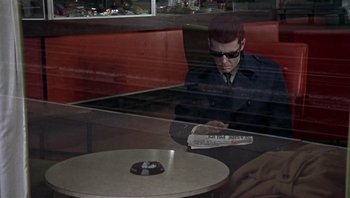 Movie still from “Performance” (1970), directed by Donald Cammell – A man sitting at a table reading a newspaper; Wide shot, High angle