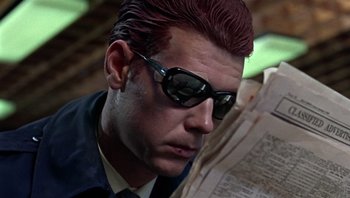 Movie still from “Performance” (1970), directed by Donald Cammell – A man in a suit and sunglasses reading a newspaper; Close Up shot, Low angle