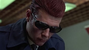 Movie still from “Performance” (1970), directed by Donald Cammell – A person wearing a suit and sunglasses; Close Up shot, Low angle