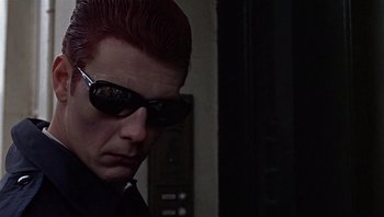 Movie still from “Performance” (1970), directed by Donald Cammell – A man with red hair wearing sunglasses and a black shirt; Close Up shot, Low angle