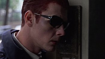 Movie still from “Performance” (1970), directed by Donald Cammell – A person wearing a suit and sunglasses; Close Up shot, Low angle