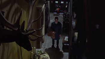 Movie still from “Performance” (1970), directed by Donald Cammell – A man standing in a hallway holding a brown bag; Wide shot, Low angle