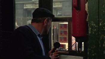 Movie still from “Performance” (1970), directed by Donald Cammell – A man holding a microphone in front of a window; Medium shot, High angle