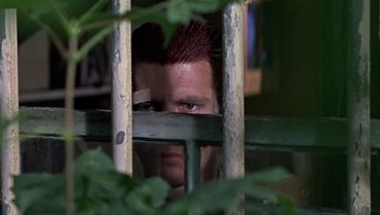 Movie still from “Performance” (1970), directed by Donald Cammell – A man with red hair looking through a metal fence; Close Up shot, Low angle