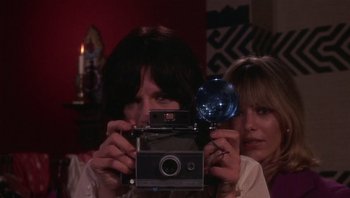Movie still from “Performance” (1970), directed by Donald Cammell – A woman taking a picture with a camera in front of another woman; Close Up shot, Low angle