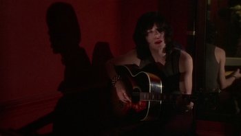 Movie still from “Performance” (1970), directed by Donald Cammell – A woman playing an acoustic guitar in a dark room; Medium shot, High angle