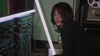 Movie still from “Performance” (1970), directed by Donald Cammell – A man sitting in front of a computer monitor; Medium shot, Low angle