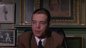 Movie still from “Performance” (1970), directed by Donald Cammell – A man wearing a suit and tie sitting in front of a painting; Close Up shot, Low angle