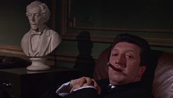 Movie still from “Performance” (1970), directed by Donald Cammell – A man sitting in a chair smoking a cigarette; Close Up shot, Low angle