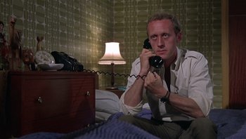 Movie still from “Performance” (1970), directed by Donald Cammell – A man sitting on a bed talking on a phone; Medium shot, Low angle
