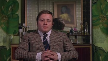 Movie still from “Performance” (1970), directed by Donald Cammell – A man sitting in a chair wearing a suit and tie; Medium shot, Low angle