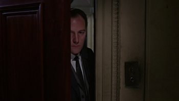 Movie still from “Performance” (1970), directed by Donald Cammell – A man wearing a suit and tie standing next to a door; Close Up shot, Low angle