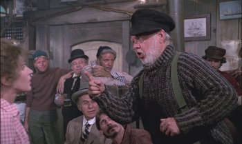 Movie still from “Pete's Dragon” (1977), directed by Don Chaffey – An old man with a beard and a hat is talking to a group of people; Medium shot, Over the shoulder angle
