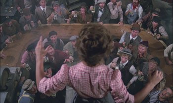 Movie still from “Pete's Dragon” (1977), directed by Don Chaffey – A crowd of people are gathered around a woman; Wide shot, Over the shoulder angle