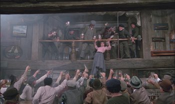 Movie still from “Pete's Dragon” (1977), directed by Don Chaffey – A group of people standing on a stage with cups; Wide shot, Low angle