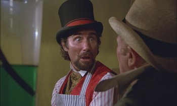 Movie still from “Pete's Dragon” (1977), directed by Don Chaffey – A man wearing a top hat talking to another man wearing an apron; Close Up shot, Over the shoulder angle
