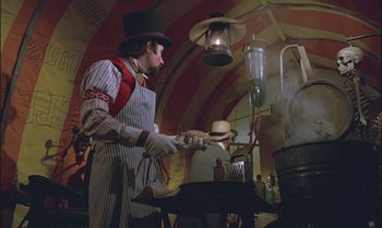 Movie still from “Pete's Dragon” (1977), directed by Don Chaffey – A man in a top hat and apron cooking food in a kitchen; Medium shot, Low angle