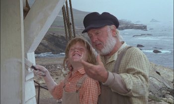 Movie still from “Pete's Dragon” (1977), directed by Don Chaffey – An older man and a young girl standing next to each other near the ocean; Medium shot, Low angle