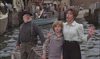 Movie still from “Pete's Dragon” (1977), directed by Don Chaffey – An older man , a young boy and an older woman are standing in front of a boat; Medium shot, Over the shoulder angle