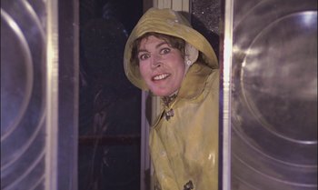 Movie still from “Pete's Dragon” (1977), directed by Don Chaffey – A woman wearing a yellow raincoat standing next to a window; Close Up shot, Low angle