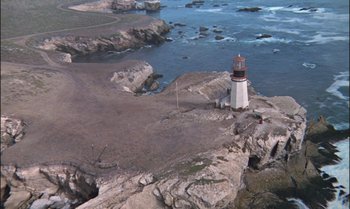 Movie still from “Pete's Dragon” (1977), directed by Don Chaffey – An aerial view of a lighthouse on a rocky shore; Extreme Wide shot, High angle