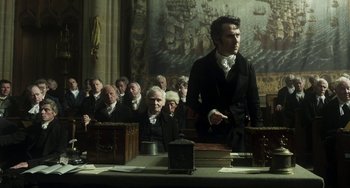 Movie still from “Peterloo” (2018), directed by Mike Leigh – A group of people sitting in front of a table; Medium shot, High angle