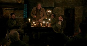 Movie still from “Peterloo” (2018), directed by Mike Leigh – A group of people sitting around a table with lit candles on it; Medium shot, Over the shoulder angle