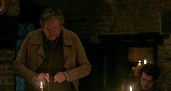 Movie still from “Peterloo” (2018), directed by Mike Leigh – An old man standing next to two lit candles; Medium shot, Over the shoulder angle