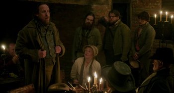 Movie still from “Peterloo” (2018), directed by Mike Leigh – A group of people standing around a table with candles; Medium shot, Over the shoulder angle