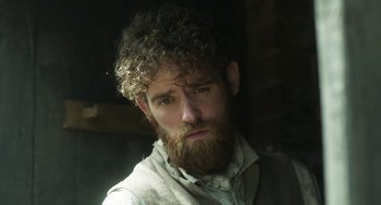 Movie still from “Peterloo” (2018), directed by Mike Leigh – A man with curly hair and a beard looking at the camera; Close Up shot, Low angle