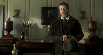 Movie still from “Peterloo” (2018), directed by Mike Leigh – A man in a suit and hat standing in front of a painting; Medium shot, Low angle