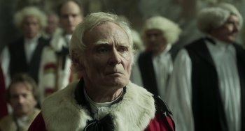 Movie still from “Peterloo” (2018), directed by Mike Leigh – An old man wearing a white wig and a red and white outfit; Close Up shot, Over the shoulder angle