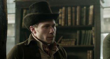 Movie still from “Peterloo” (2018), directed by Mike Leigh – A man wearing a hat and a bow tie in front of a book shelf; Close Up shot, Low angle