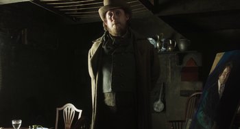 Movie still from “Peterloo” (2018), directed by Mike Leigh – A man wearing a hat and a long coat standing next to a chair; Medium shot, Low angle