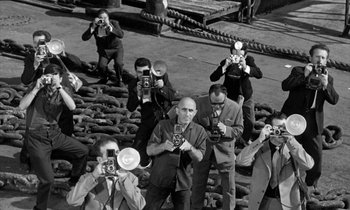 Movie still from “Phaedra” (1962), directed by Jules Dassin – A black and white photo of a group of people taking pictures; Wide shot, High angle