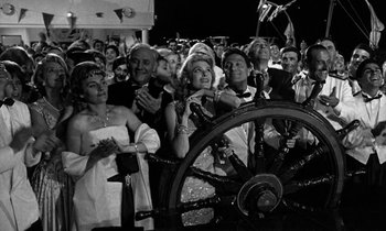 Movie still from “Phaedra” (1962), directed by Jules Dassin – A group of people standing next to each other in front of a steering wheel; Wide shot, High angle