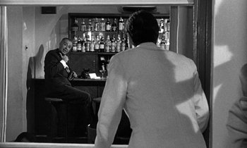 Movie still from “Phaedra” (1962), directed by Jules Dassin – A black and white photo of a man in a suit looking in a mirror; Medium shot, Over the shoulder angle