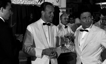 Movie still from “Phaedra” (1962), directed by Jules Dassin – A black - and - white photo of men in tuxedos holding drinks; Medium shot, Low angle