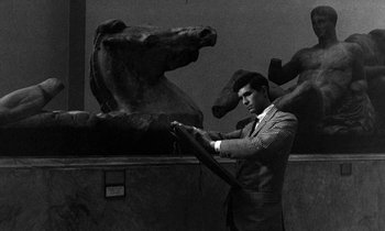 Movie still from “Phaedra” (1962), directed by Jules Dassin – A black and white photo of a man in front of a statue; Medium shot, High angle