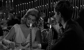 Movie still from “Phaedra” (1962), directed by Jules Dassin – A man and a woman sitting in front of candles; Medium shot, Over the shoulder angle