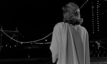 Movie still from “Phaedra” (1962), directed by Jules Dassin – A black and white photo of a woman standing in front of a bridge; Medium shot, Low angle