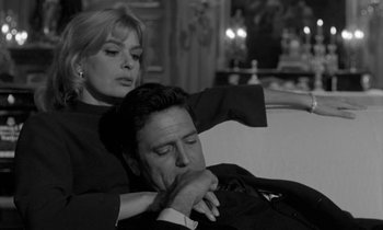 Movie still from “Phaedra” (1962), directed by Jules Dassin – A man and a woman sitting on a couch together; Medium shot, Low angle