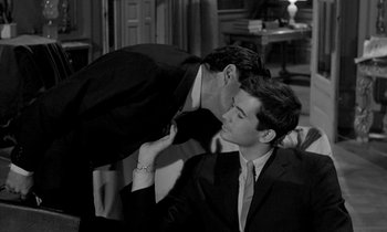 Movie still from “Phaedra” (1962), directed by Jules Dassin – A man in a suit kissing another man in a suit; Medium shot, Over the shoulder angle