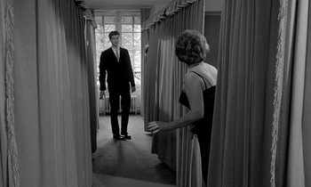 Movie still from “Phaedra” (1962), directed by Jules Dassin – A man and a woman are standing in a hallway; Wide shot, Over the shoulder angle