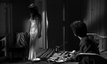 Movie still from “Phaedra” (1962), directed by Jules Dassin – A woman standing in front of a man at a table; Medium shot, Over the shoulder angle