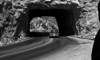 Movie still from “Phaedra” (1962), directed by Jules Dassin – Black and white photograph of a car driving through a tunnel; Extreme Wide shot, High angle