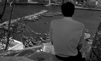 Movie still from “Phaedra” (1962), directed by Jules Dassin – A man sitting on a ledge looking out over a harbor; Wide shot, High angle